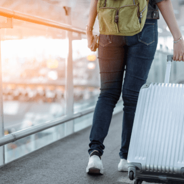 mulher de calça jeans e mochila verde com uma mala prateada no aeroporto