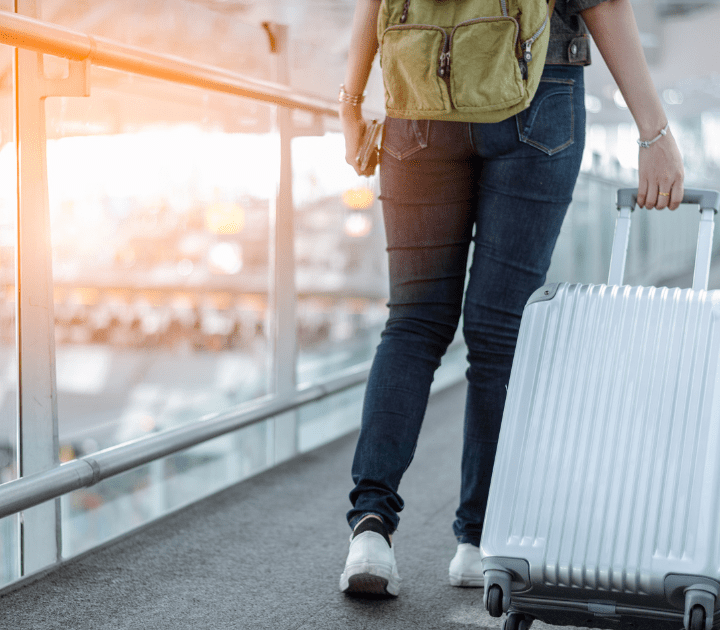 mulher de calça jeans e mochila verde com uma mala prateada no aeroporto