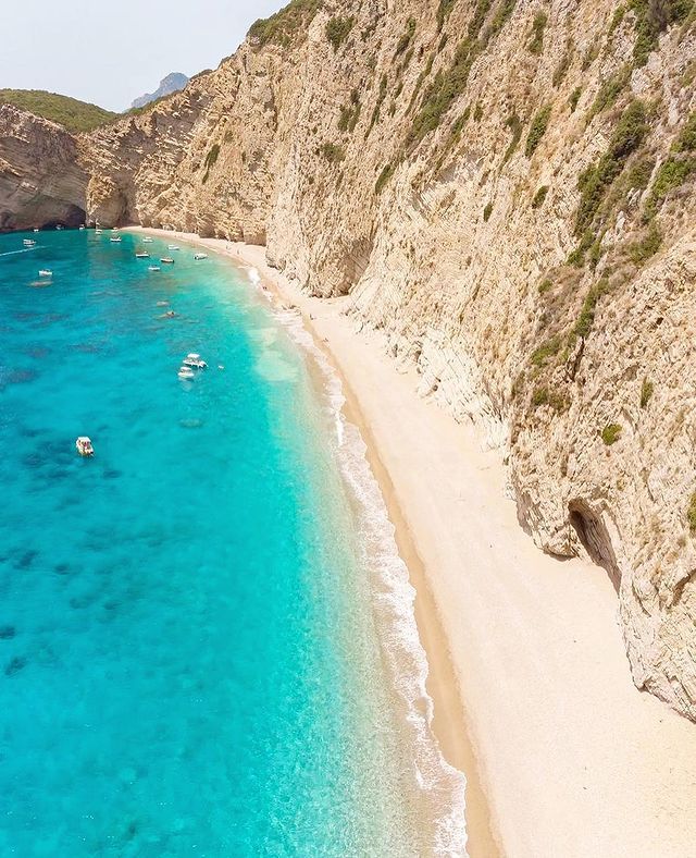 Paradise Beach, a praia de Corfu mais famosa. Mar cristalino e falésia branca de pedras. Pequenos barcos ancorados no mar.
